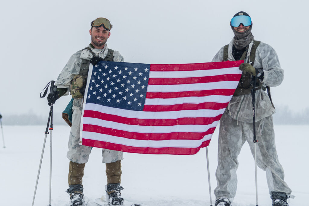 Connor McNeil, left, holds the U.S. flag with a fellow solider just after conducting a mission in which they fended off a mock attack on snowmobiles and skis.