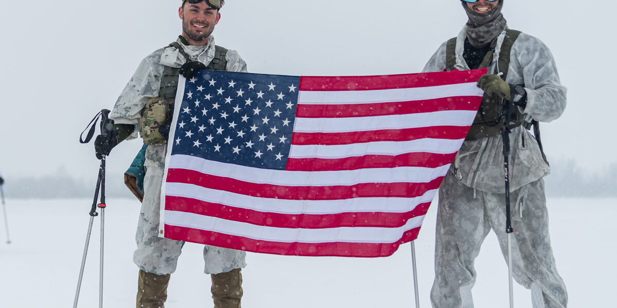 Connor McNeil, left, holds the U.S. flag with a fellow solider just after conducting a mission in which they fended off a mock attack on snowmobiles and skis.
