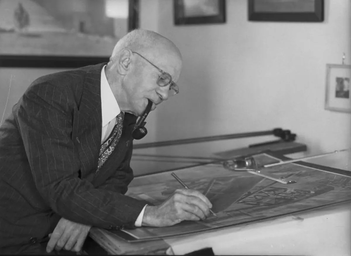 A man in a suit and glasses, with a pipe in his mouth, draws architectural plans at a drafting table in an office.